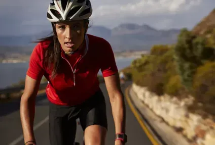 Cyclist in a helmet and red jersey riding hard on a coastal road