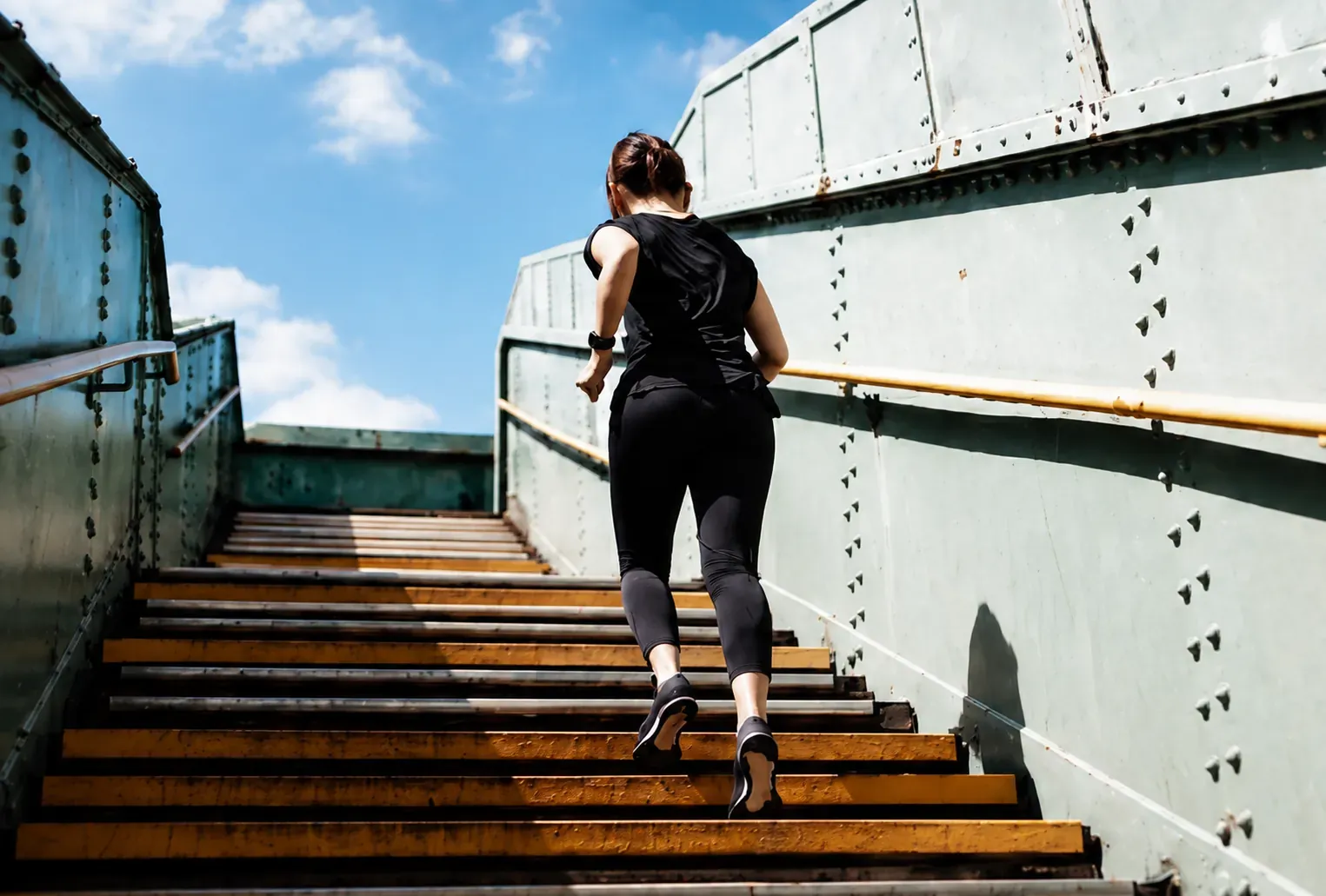 Runner in black athletic wear climbing a steel bridge staircase