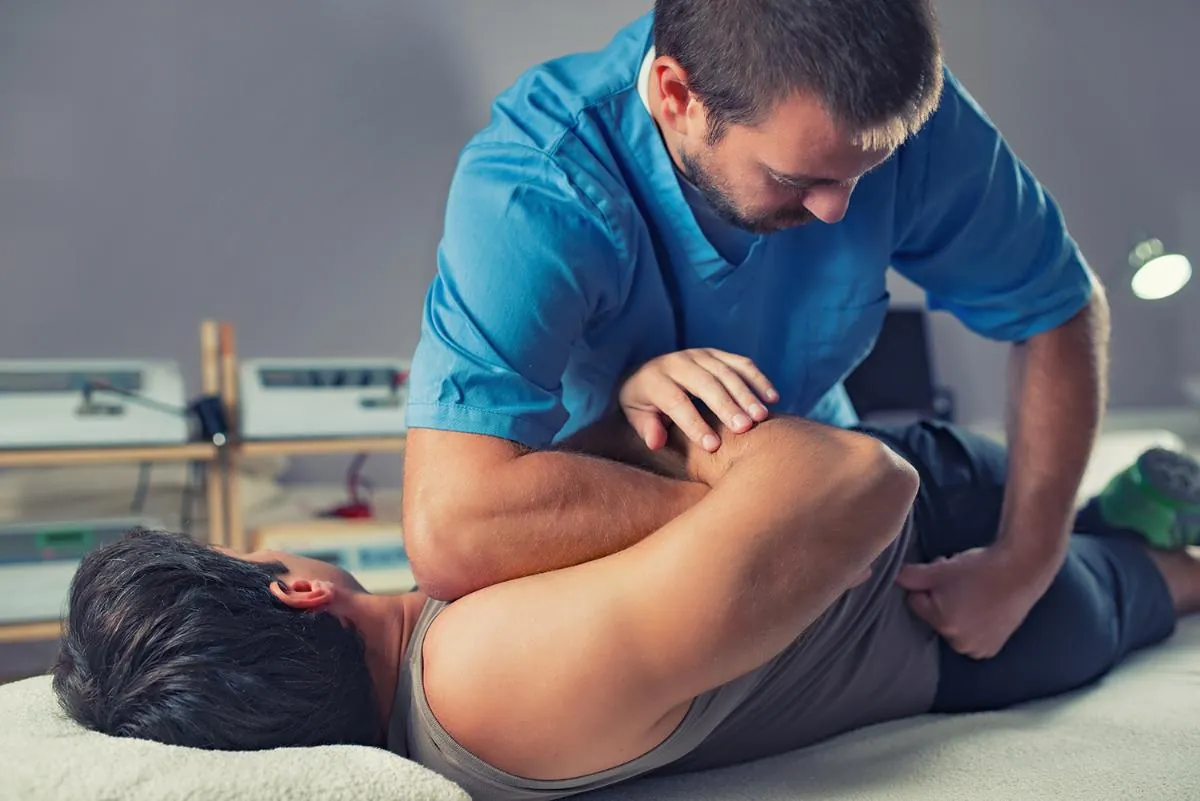 Practitioner in teal scrubs performing a hands-on adjustment on a patient lying on a table