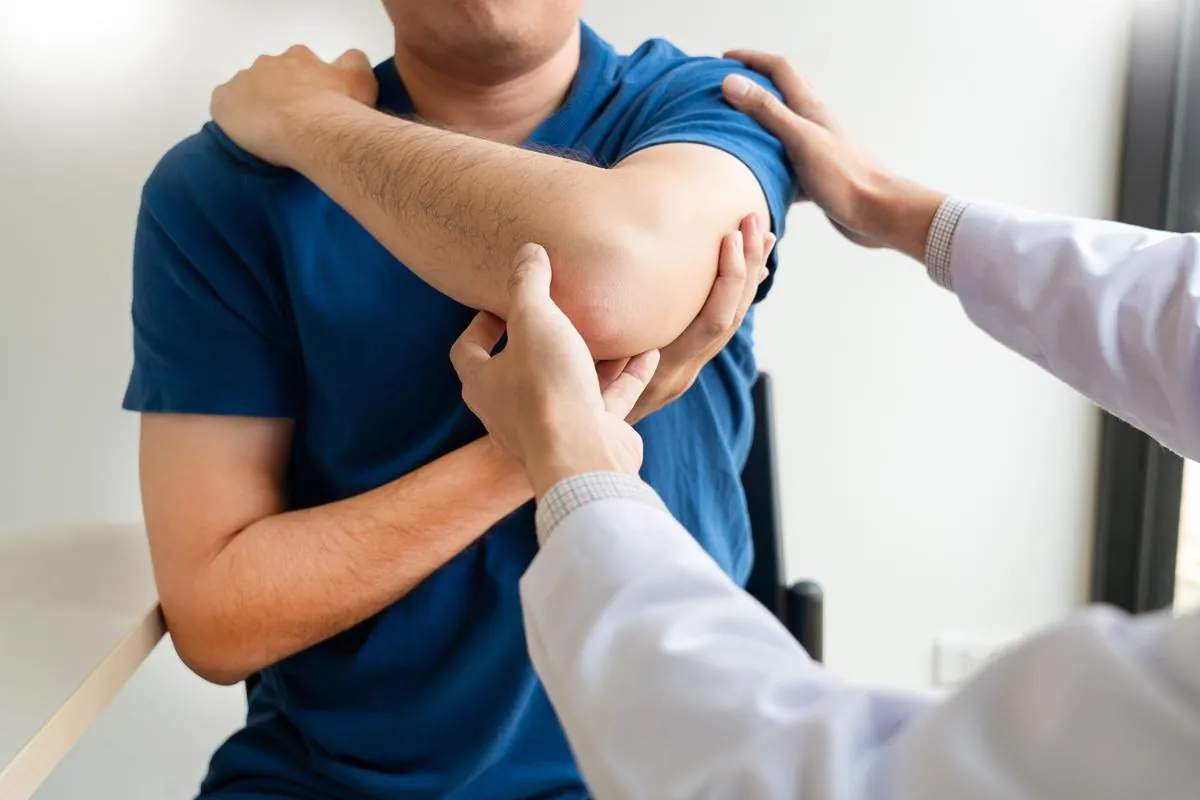 Doctor in a white coat moving a patient's arm during a shoulder exam