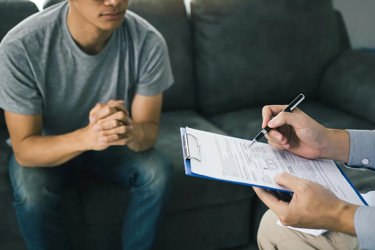 Patient sitting on a couch while a clinician writes on an intake form on a clipboard