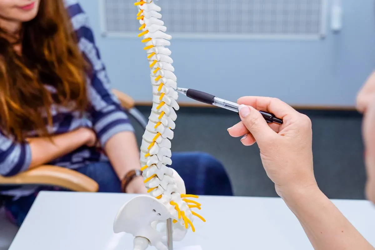 Clinician pointing a pen at a spine model while a patient looks on