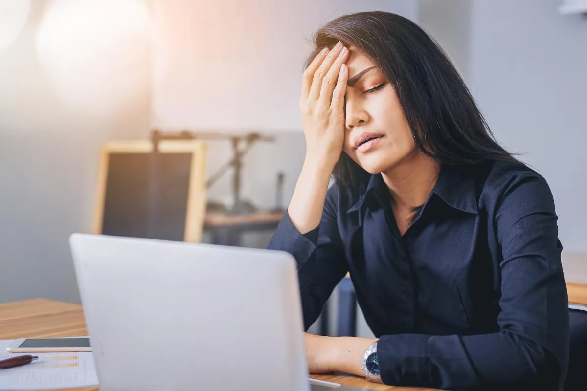 Woman at a laptop with her hand pressed to her forehead