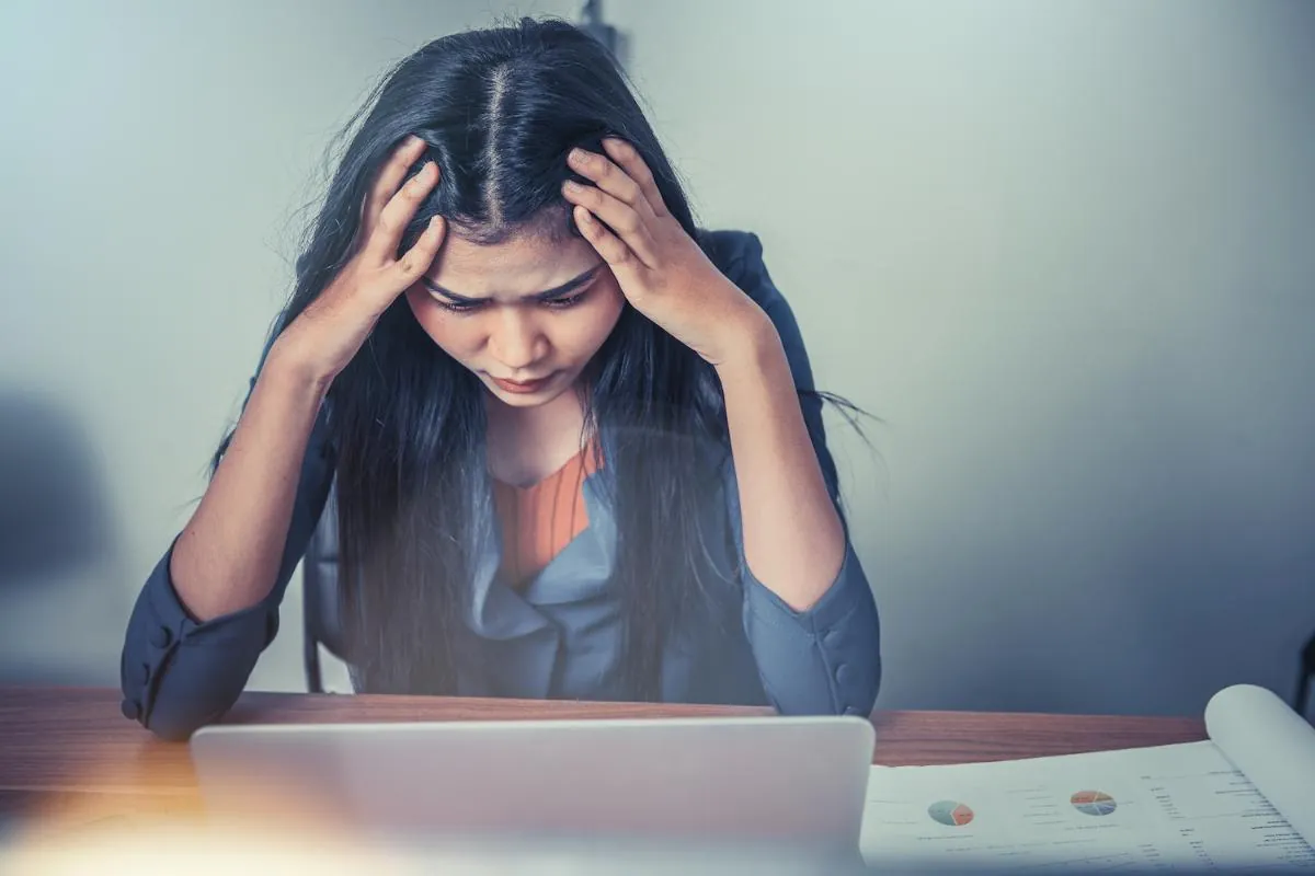 Woman at a laptop holding her head in both hands