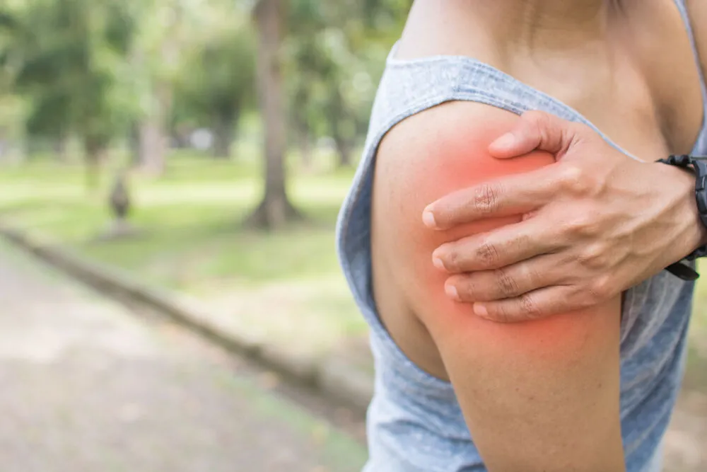 Person holding their upper arm with the shoulder area highlighted in red outdoors