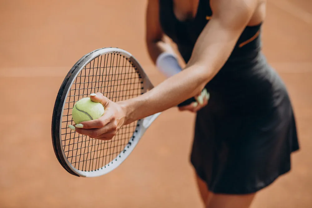 Tennis player in a black dress holding a racket and ball on a clay court