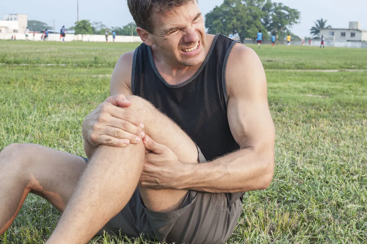 Man sitting on grass grimacing and gripping his knee