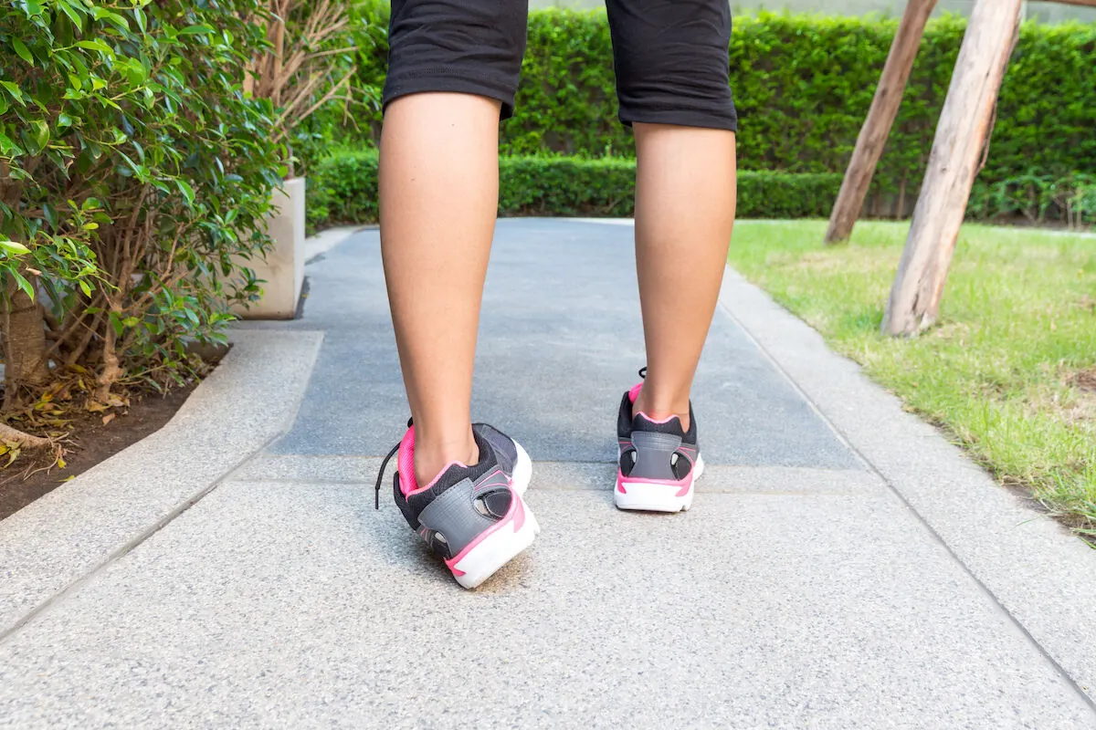Legs and pink-and-gray sneakers of a person walking on a garden path