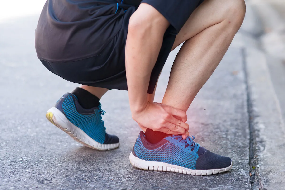 Runner crouching on a path holding an ankle highlighted in red