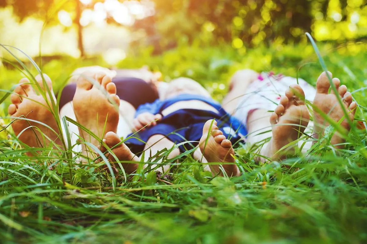 People lying in tall green grass seen from their bare feet